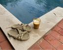 Rope sandals and a glass of iced coffee by a poolside.